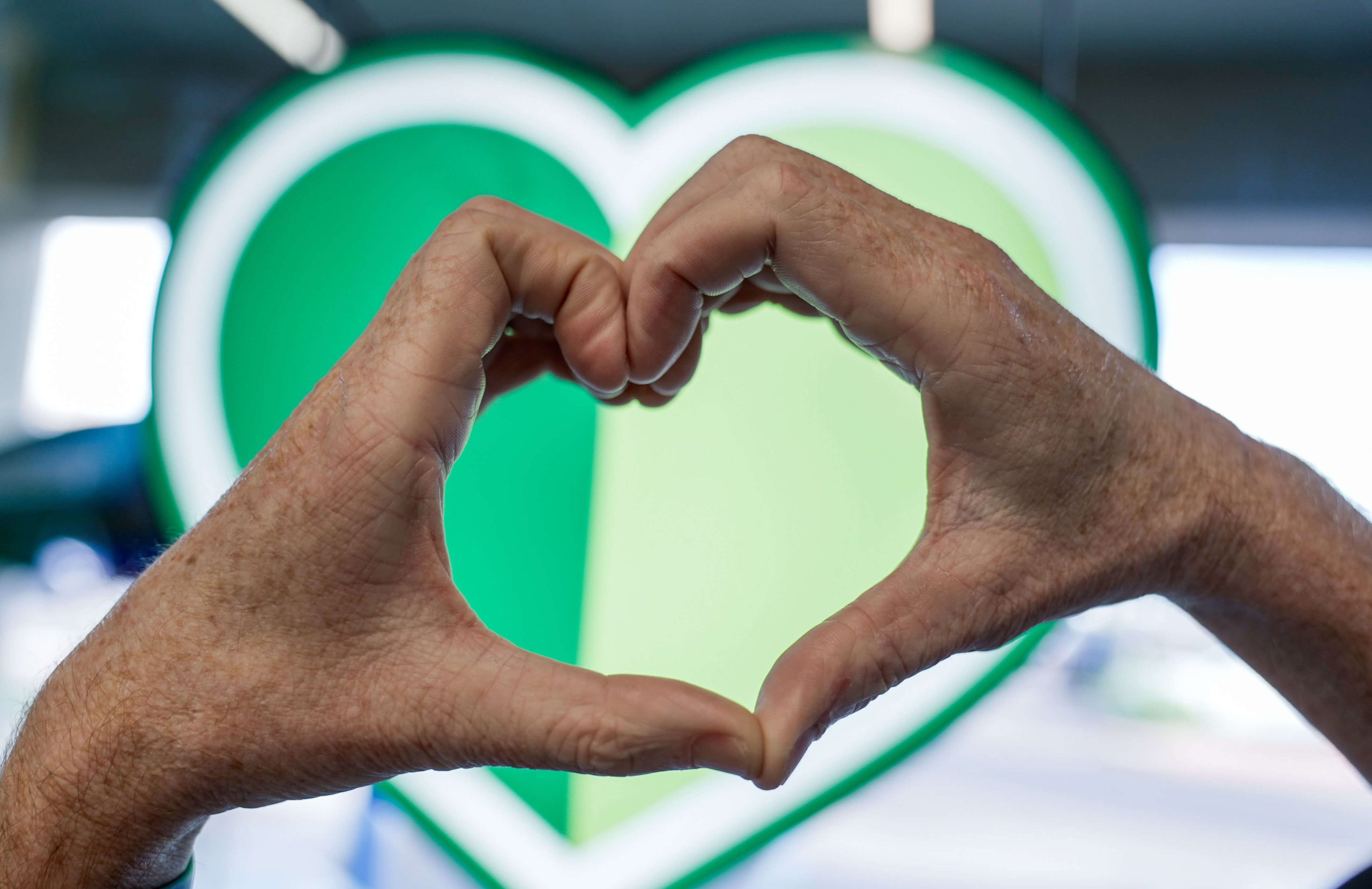 Hands forming a heart shape in front of a large green heart background.